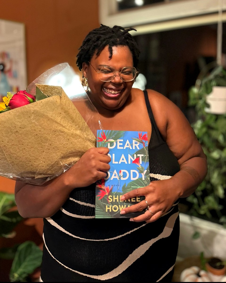 Shenee laughing, holding flowers and her novel Dear Plant Daddy
